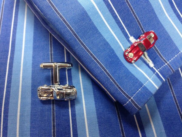 Two Vintage Car Cufflinks next to a toy car on a blue striped fabric surface.