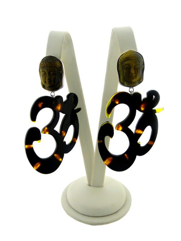 A pair of earrings with Buddha head studs and dangling OM Resin Earrings, displayed on a white stand against a light background.