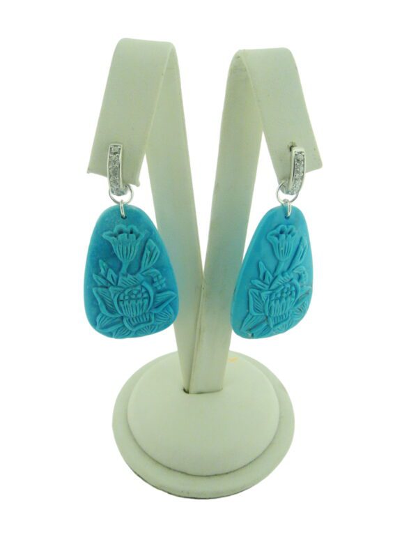 A pair of Carved Turquoise Earrings with floral designs hanging on a white display stand.