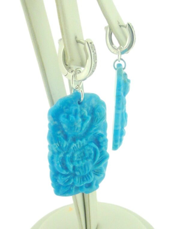 A pair of Carved Turquoise Earrings hanging from a metal stand with a white background.