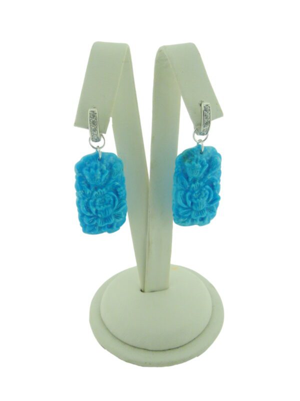 A pair of Carved Turquoise Earrings displayed on a white stand.