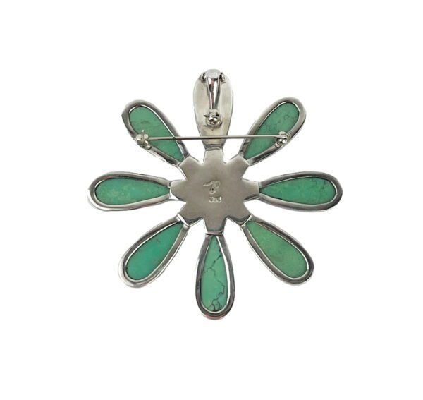 A silver and green flower pendant with a pin.