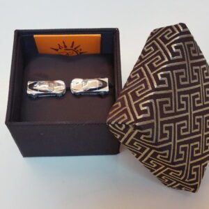 A pair of Carved Turquose Floral Cufflinks in a box beside a patterned necktie on a white surface.