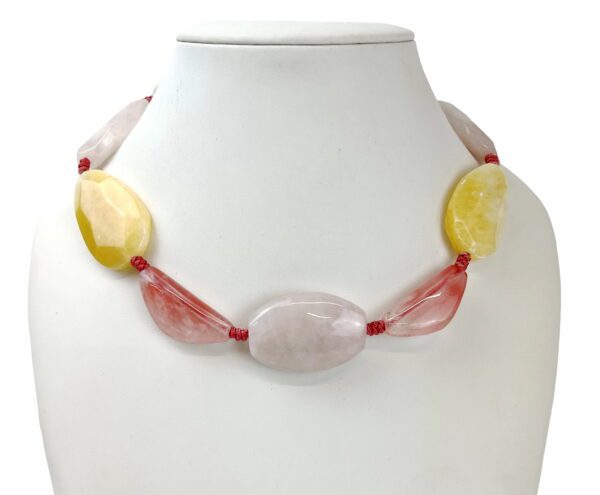 A necklace of yellow and red beads on a white bust.