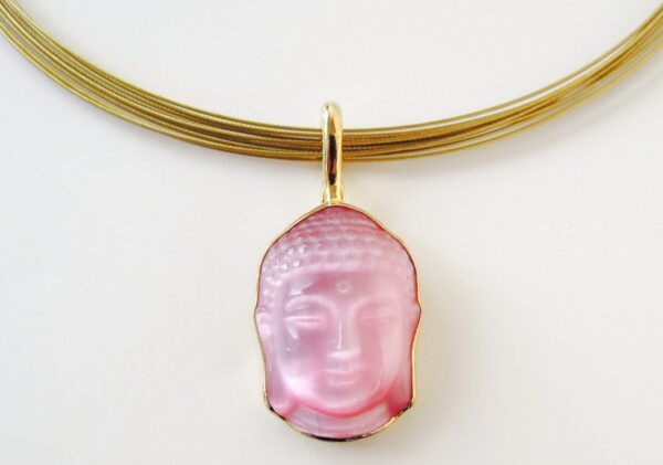 A pink Supreme pendant hangs from a gold multi-strand necklace against a white background.