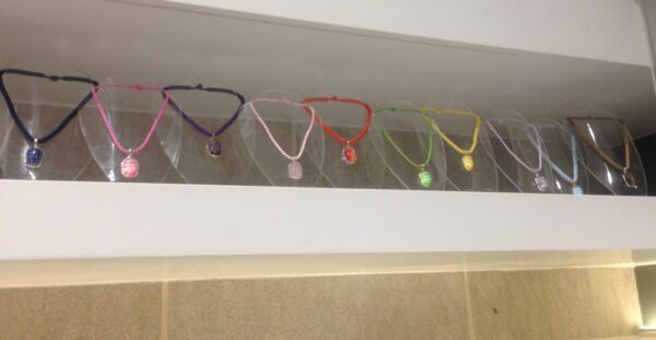 A row of colorful necklaces with Buddha pendants displayed on a shelf under bright lighting.