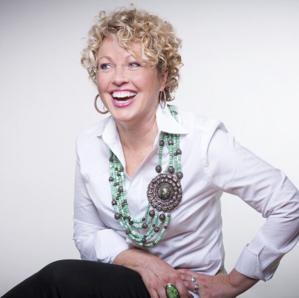 A woman with curly hair wearing a necklace and smiling.