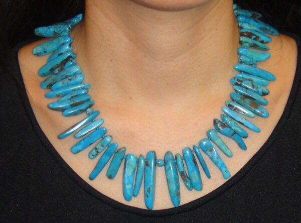 A woman wearing a necklace with turquoise colored beads.