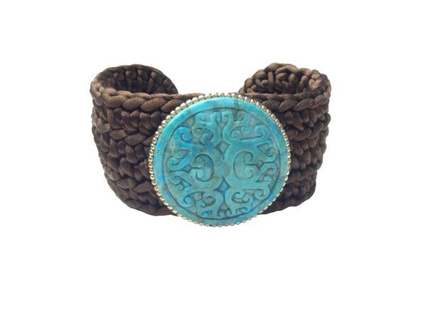 Brown braided leather bracelet with a large Carved Turquoise Flexible centerpiece in a decorative silver setting, isolated on a white background.