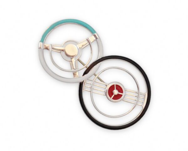 Two Double Steering Wheel Brooches, one with teal and silver accents, the other with black and red, both on a white background.